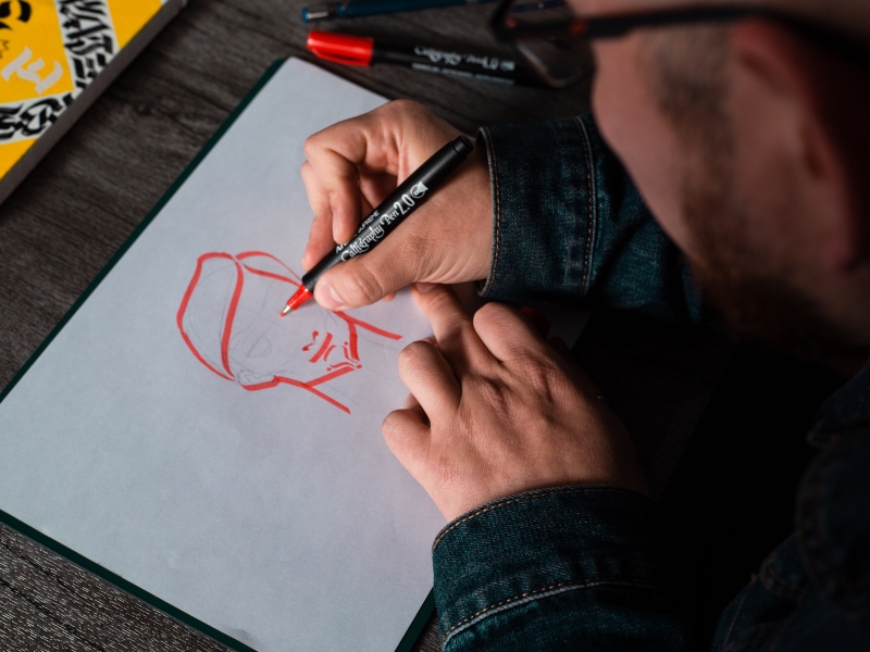 A photograph of someone drawing with a red calligraphy pen