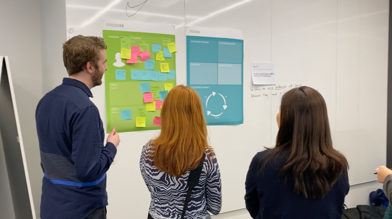Three people participating in a workshop, looking at several post-its on a whiteboard